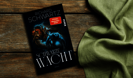 „Schwarze Wacht“ von Richard Schwartz liegt auf Holz neben grünem Stoff.