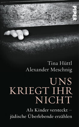 Das Buchcover zeigt einen schwach beleuchteten, fast monochromen Hintergrund, der in Schwarz- und Grautönen gehalten ist. Im Vordergrund ist eine zarte Hand zu sehen, die an einer Kante lehnend nach oben greift, was ein Gefühl von Hoffnung und Widerstand vermittelt. Der Titel „UNS KRIEGT IHR NICHT“ ist in kräftig grauer Schrift zentriert und sticht durch seine elegante Typografie hervor. Darunter steht in kleinerer Schrift der Untertitel: „Als Kinder versteckt – jüdische Überlebende erzählen“. Die Namen der Autoren, Tina Hüttl und Alexander Meschnig, erscheinen darüber.
