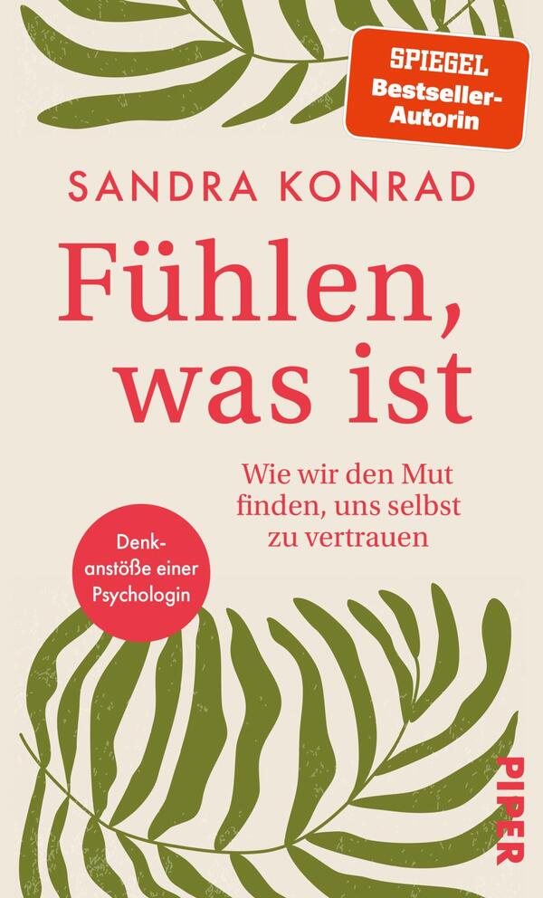 Das Buchcover zeigt einen hellen, neutralen Hintergrund mit grünen Blattmotiven, die eine entspannte Atmosphäre vermitteln. Der Titel „Fühlen, was ist“ ist zentral platziert und in kräftigem Rot gehalten, während der Untertitel „Wie wir den Mut finden, uns selbst zu vertrauen“ in kleinerer Schrift darunter steht. Oben links befindet sich der Name der Autorin Sandra Konrad, und ein rotes Rechteck mit dem Hinweis „SPIEGEL Bestseller-Autorin“ hebt sich deutlich ab. Unten links ist ein runder Sticker in gedecktem Rot mit dem Text „Denkanstoß einer Psychologin“ zu sehen.