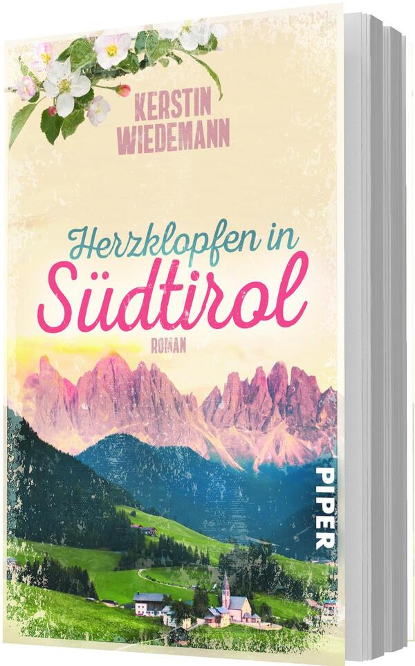 Das Buchcover zeigt eine idyllische Südtirol-Landschaft mit grünen Almen, einem kleinen Dorf mit Kirche im Vordergrund und rosé-illuminierten Dolomiten im Hintergrund. Oben links blüht ein Ast mit weißen Blumen. Auf cremefarbenem, leicht strukturiertem Grund steht der Autorenname „Kerstin Wiedemann“ in Großbuchstaben, darüber der Titel „Herzklopfen in Südtirol“ in zweifarbiger Schrift (türkis Script und großes pinkes Script). Stimmung: romantisch und warm.
