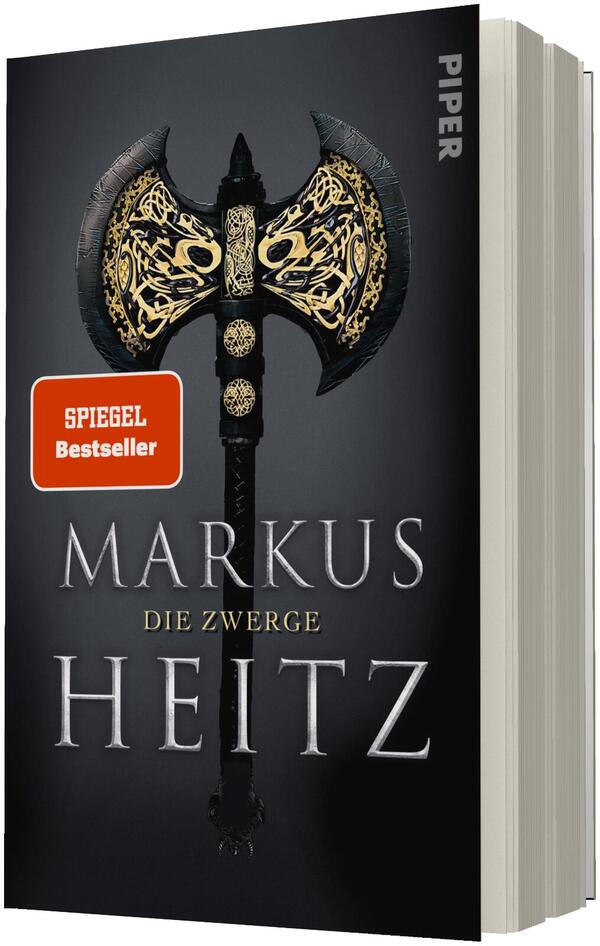 Das Buchcover zeigt einen dunklen, nahezu schwarzen Hintergrund mit zentral platzierter zweischneidiger Streitaxt, deren Äxteköpfe mit goldenen, keltisch wirkenden Ornamenten verziert sind. Der Autorenname „Markus Heitz“ steht groß in silbrig-metallischer Serifenschrift, darunter der Untertitel „Die Zwerge“ in kleinerer goldener Schrift. Ein orangefarbener rechteckiger Sticker trägt den Text „SPIEGEL Bestseller“. Atmosphäre: düster, episch, mittelalterlich.