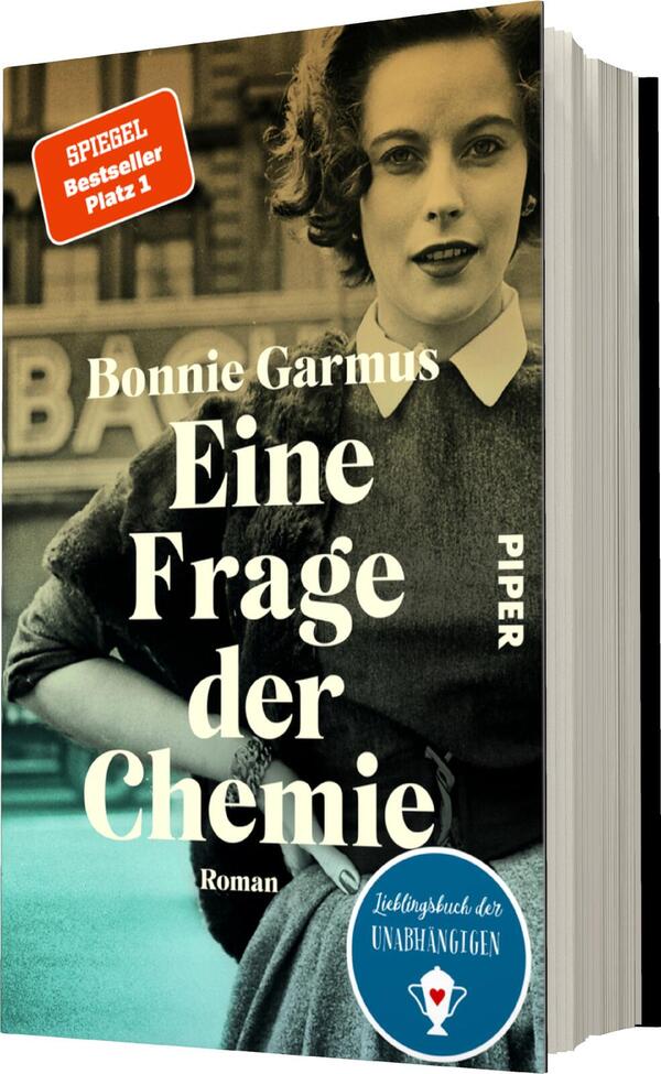 Das Buchcover zeigt eine schwarz-weiß gehaltene Portraitaufnahme einer Frau mit lockigem Haar, die in einem modernen, eleganten Kleid erscheint. Ihr Blick ist selbstbewusst, und sie steht vor einem urbanen Hintergrund. Der Titel „Eine Frage der Chemie“ ist im Zentrum in großen, weißen Buchstaben platziert, darunter steht „Roman“ in kleinerer Schrift. Der Name „Bonnie Garmus“ ist darüber und ebenso gut lesbar. In der oberen linken Ecke befindet sich ein rotes Etikett mit der Aufschrift „SPIEGEL Bestseller Platz 1“. Am unteren Rand ist ein blauer Kreis mit dem Text „Lieblingsbuch der Unabhängigen“ zu sehen.