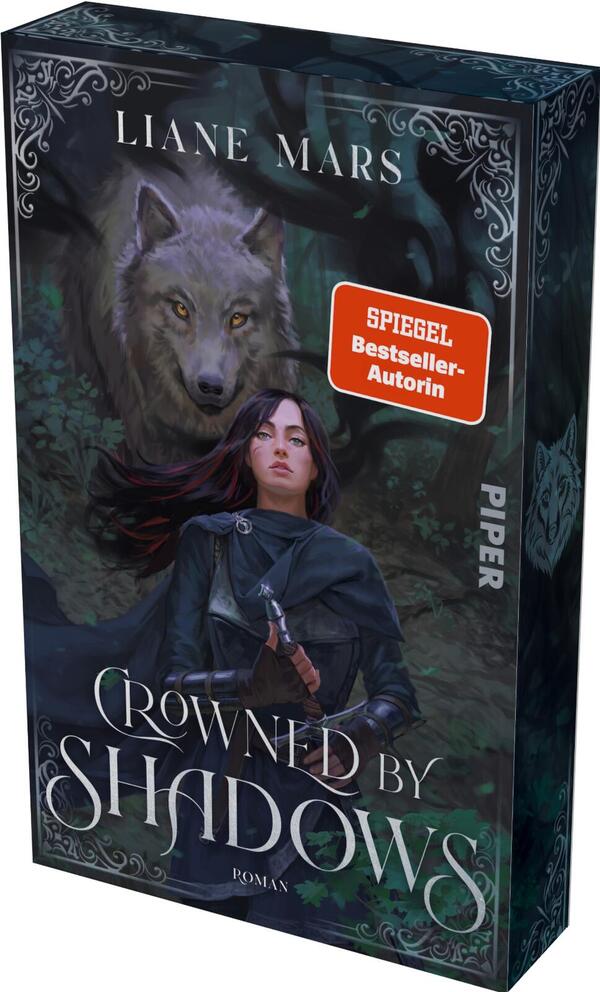 Das Buchcover zeigt eine junge Frau in dunklem Umhang, die einen Dolch vor der Brust hält; hinter ihr ein großer grauer Wolf mit gelben Augen, beide vor einem dunklen, nebeligen Wald. Farbgebung: tiefe Blaugrün-, Grau- und Schwarztöne mit dezenten Violettakzenten. Oben steht „LIANE MARS“ in klarer Versal-Serif, unten der Titel „Crowned by Shadows“ in geschwungener Serifschrift. Rechts ein roter Aufkleber „SPIEGEL Bestseller-Autorin“. Stimmung: geheimnisvoll und bedrohlich.
