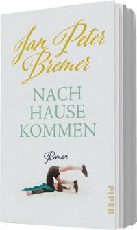 Das Buchcover zeigt den Titel „NACH HAUSE KOMMEN“ in eleganter, grüner Schrift, die mittig platziert ist. Darunter steht in kleinerer, grauer Schrift das Wort „Roman“. Der Autorname „Jan Peter Bremer“ ist in geschwungener, goldener Schrift oben auf dem Cover positioniert. Im unteren Bereich ist eine stilisierte Illustration einer Person zu sehen, die in einer dynamischen Pose auf dem Boden liegt, umgeben von einem türkisfarbenen Tuch. Der Hintergrund ist hell und lädt zur Betrachtung ein.