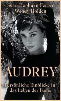 Das Buchcover zeigt eine Schwarz-Weiß-Fotografie von einer Frau mit einem sanften Lächeln, umgeben von grünen Olivenzweigen. Sie trägt einen schwarzen Rollkragenpullover und blickt direkt in die Kamera. Der Titel „AUDREY“ ist in großen, goldenen Buchstaben in der Mitte platziert, darunter steht der Untertitel „Persönliche Einblicke in das Leben der Ikone“ in kleinerer, heller Schrift. Die beiden Autoren, Sean Hepburn Ferrer und Wendy Holden, sind oben in eleganter, weißer Schrift angeführt. Die Atmosphäre ist nostalgisch und stilvoll.