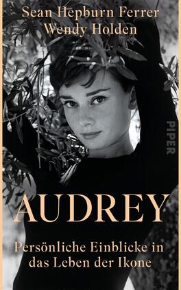 Das Buchcover zeigt eine Schwarz-Weiß-Fotografie von einer Frau mit einem sanften Lächeln, umgeben von grünen Olivenzweigen. Sie trägt einen schwarzen Rollkragenpullover und blickt direkt in die Kamera. Der Titel „AUDREY“ ist in großen, goldenen Buchstaben in der Mitte platziert, darunter steht der Untertitel „Persönliche Einblicke in das Leben der Ikone“ in kleinerer, heller Schrift. Die beiden Autoren, Sean Hepburn Ferrer und Wendy Holden, sind oben in eleganter, weißer Schrift angeführt. Die Atmosphäre ist nostalgisch und stilvoll.