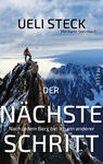 Das Buchcover zeigt einen Bergsteiger in rot-orangefarbener Bekleidung, der sich auf einem schneebedeckten Gipfel befindet. Im Hintergrund sind majestätische, schneebedeckte Berge und ein klarer blauer Himmel zu sehen. Der Titel „DER NÄCHSTE SCHRITT“ erscheint in großer, weißer Schrift, während der Untertitel „Nach jedem Berg bin ich ein anderer“ in kleinerer, grauer Schrift darunter steht. Der Name des Autors „Ueli Steck“ steht oben links in schwarzer Schrift, ergänzt durch den Verweis auf die Mitautorin „Karin Steinbach“. Das Verlagslogo „MALIK“ ist in kleiner Schrift unten rechts platziert.