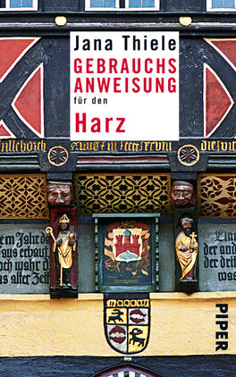 Das Buchcover zeigt die historische Fassade eines Fachwerkhauses im Harz, reich verziert mit Schnitzereien und farbigen Elementen in Rot, Schwarz und Gold. Der Titel „GEBRAUCHSANWEISUNG für den Harz“ ist in markanter Schrift in Weiß und Rot positioniert. Darunter steht der Name der Autorin, Jana Thiele, in einer klaren, eleganten Schrift. Die Gestaltung vermittelt eine traditionelle und kulturelle Atmosphäre, die das Thema des Buches widerspiegelt.