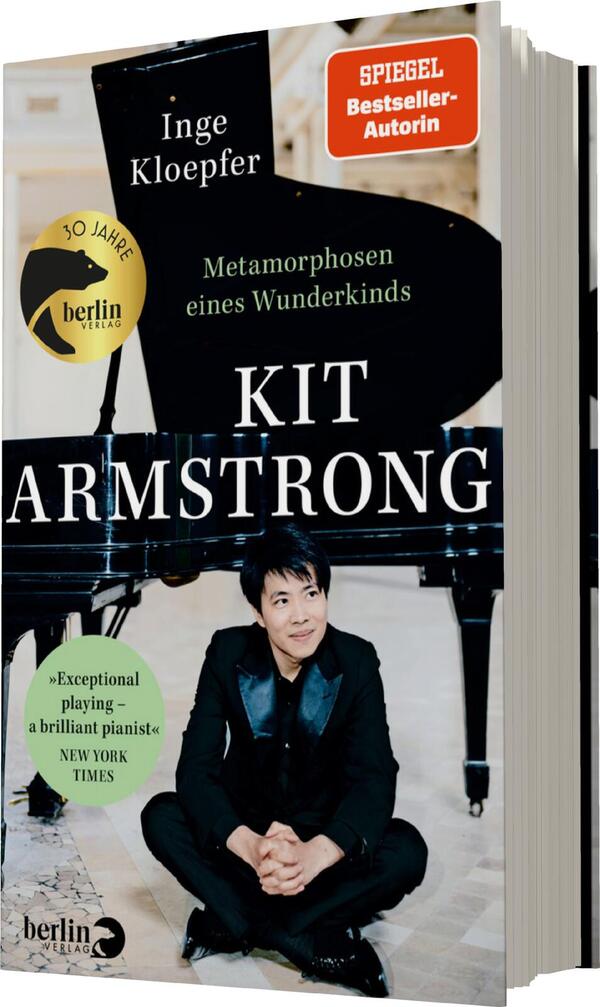 Das Buchcover zeigt einen jungen Pianisten, der auf einem Klavier sitzt. Er trägt ein schwarzes Outfit mit einer blauen Jacke und lächelt in die Kamera. Der Hintergrund ist hell und erzeugt eine freundliche Atmosphäre. Oben links steht der Name der Autorin „Inge Kloepfer“, daneben die Auszeichnung „SPIEGEL-Bestseller-Autorin“. In der Mitte prangt der Titel „KIT ARMSTRONG“ in großen, weißen Buchstaben. Unter dem Titel steht der Untertitel „Metamorphosen eines Wunderkindes“. Am unteren Rand findet sich ein Zitat der New York Times: „Exceptional playing – a brilliant pianist“.