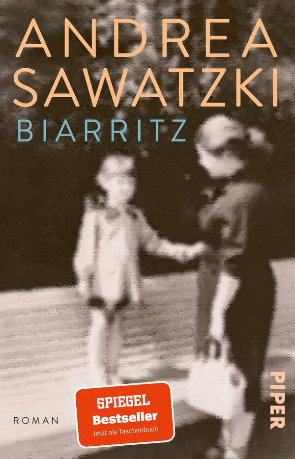 Das Buchcover zeigt ein unscharfes, sepiafarbenes Foto zweier Personen, die sich an den Händen halten, vor einem verschwommenen Hintergrund. Groß oben steht der Autorname „ANDREA SAWATZKI“ in großem, hellorangefarbenem Versalschriftzug; darunter der Titel „BIARRITZ“ in kleinerem türkisblauen Versaltext. Unten links ein oranger Sticker mit „SPIEGEL Bestseller“ und „Jetzt als Taschenbuch“, unten rechts senkrecht der Verlagstitel „PIPER“.