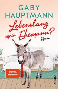 Das Buchcover zeigt eine humorvolle Szene mit einem Esel, der auf zwei Beinen steht und eine rote Krawatte trägt. Im Hintergrund ist ein modernes Schlafzimmer mit einem weißen Bett und einer hellen Wandgestaltung angedeutet. Der Titel „Lebenslang mein Ehemann?“ ist in einer verspielten, rot gefärbten Schriftart prominent platziert. Der Autorename „Gaby Hauptmann“ erscheint in einer klaren, grünen Schrift darüber. Unten links befindet sich ein rotes Kästchen mit dem Text „SPIEGEL Bestseller“.