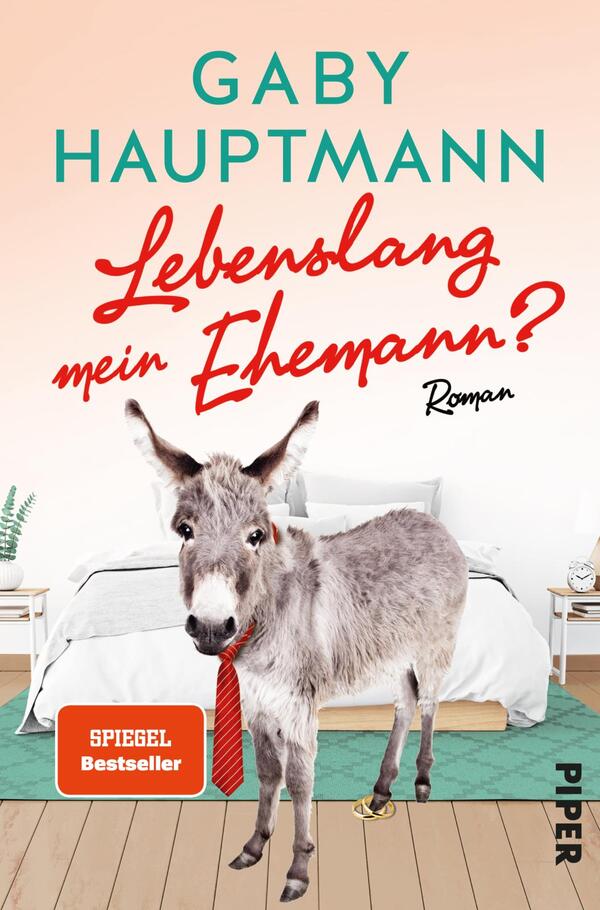 Das Buchcover zeigt eine humorvolle Szene mit einem Esel, der auf zwei Beinen steht und eine rote Krawatte trägt. Im Hintergrund ist ein modernes Schlafzimmer mit einem weißen Bett und einer hellen Wandgestaltung angedeutet. Der Titel „Lebenslang mein Ehemann?“ ist in einer verspielten, rot gefärbten Schriftart prominent platziert. Der Autorename „Gaby Hauptmann“ erscheint in einer klaren, grünen Schrift darüber. Unten links befindet sich ein rotes Kästchen mit dem Text „SPIEGEL Bestseller“.