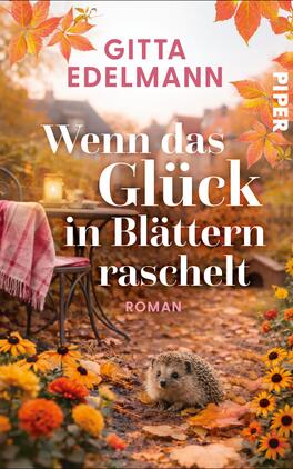 Das Buchcover zeigt eine herbstliche Gartenszene bei goldenem Licht: im Vordergrund ein Igel zwischen orange-gelben Blumen und fallenden Blättern. Links ein schmales Metall-Bistrotisch mit rosa-weißem Plaid und eine Laterne im unscharfen Hintergrund. Titel „Wenn das Glück in Blättern raschelt“ steht groß in weißer Serifenschrift, Autorenname Gitta Edelmann oben in kräftigem Pink, darunter klein „Roman“.