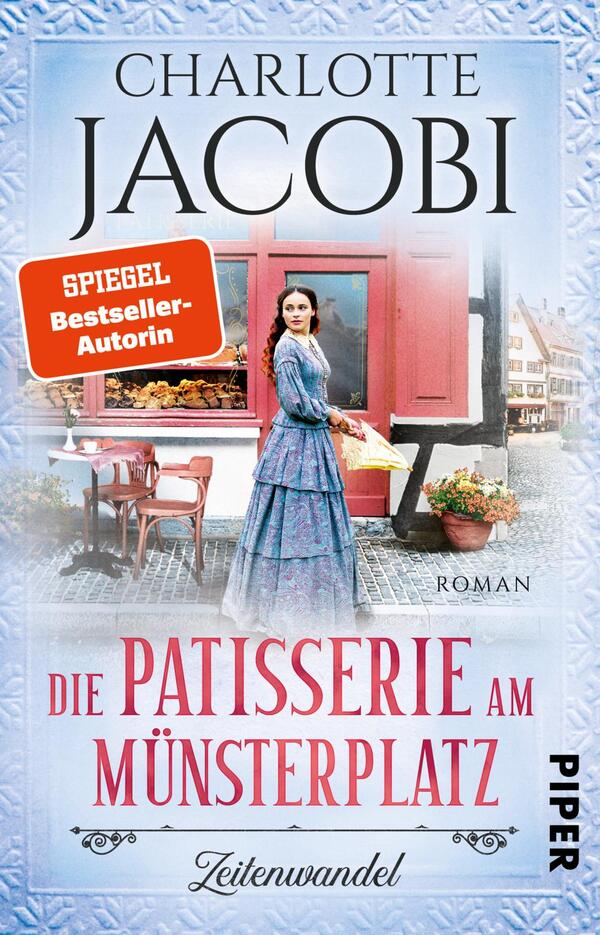 Das Buchcover zeigt eine historische Szene mit einer weiblichen Figur in einem eleganten, blauen Kleid, die vor einem charmanten, roten Patisserie-Geschäft steht. Die Atmosphäre strahlt Nostalgie und Gastronomie aus. Der Titel „Die Patisserie am Münsterplatz“ ist in geschwungener Schrift in der unteren Mitte platziert, während der Autorennamen „Charlotte Jacobi“ oben hervorgehoben wird. Ein orangefarbener Hinweis „SPIEGEL Bestseller-Autorin“ zieht die Aufmerksamkeit auf sich. Der Hintergrund ist hell und freundlich gestaltet.