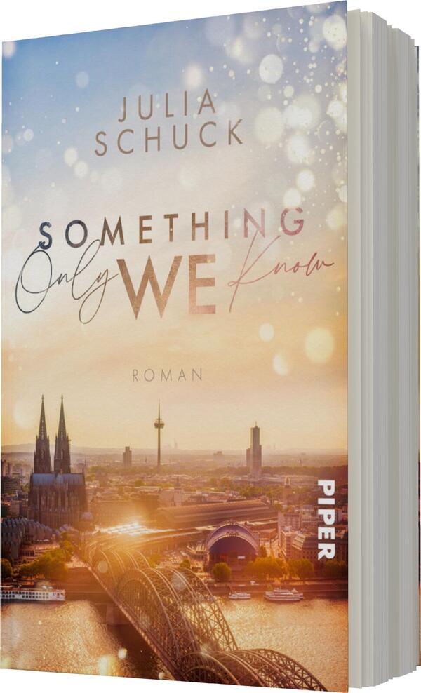 Das Buchcover zeigt eine romantische Stadtansicht von Köln bei Sonnenuntergang, mit einer weichen Farbpalette aus Pastelltönen und goldenen Glitzereffekten, die eine verträumte Atmosphäre schaffen. Der Titel „Something Only WE know“ ist in einer eleganten, gemischten Typografie gestaltet, wobei „WE“ besonders hervorgehoben ist. Der Autorennamen „Julia Schuck“ befindet sich oben auf dem Cover. Am unteren Rand steht der Hinweis „ROMAN“.