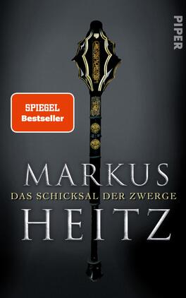 Das Buchcover zeigt einen schwarzen Hintergrund, vor dem ein beeindruckender, verzierter Stab mit goldenen Elementen thront. Oben ist der Stab kunstvoll geformt, während der untere Teil schlicht gehalten ist. In der Mitte steht der Autorennamen „MARKUS HEITZ“ in großen, silbernen Buchstaben, unterhalb befindet sich der Titel „DAS SCHICKSAL DER ZWERGE“ in ebenfalls silberner Schrift. Ein rotes Label mit dem Text „SPIEGEL Bestseller“ ist in der oberen linken Ecke platziert.