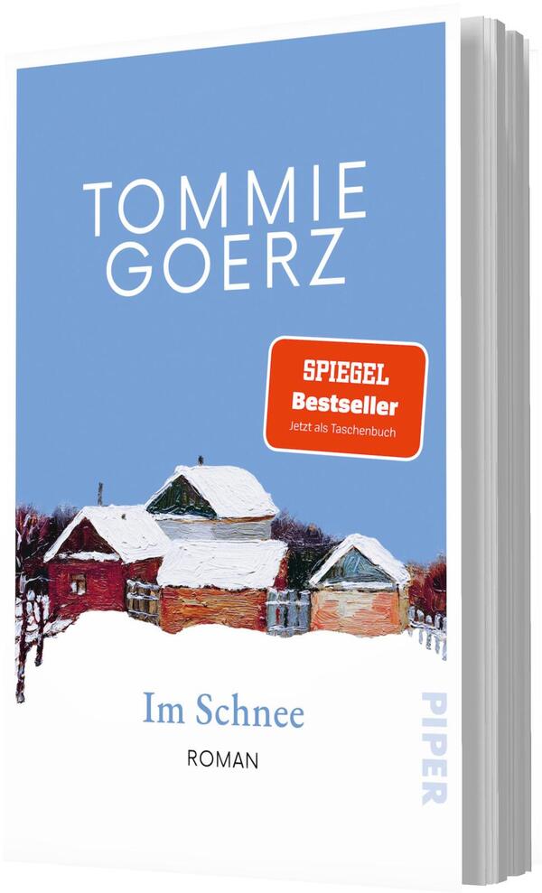 Das Buchcover zeigt oben den Autorennamen TOMMIE GOERZ in großer weißer, serifenloser Großbuchstabenschrift auf sanftem hellblauem Hintergrund. Darunter eine gemalte, impressionistische Winterlandschaft mit drei schneebedeckten Häusern in Rot‑ und Orangetönen. Rechts ein roter Badge mit der Aufschrift „SPIEGEL Bestseller – jetzt als Taschenbuch“. Unten der Titel „Im Schnee“ in blauer Schrift, darunter klein „ROMAN“. Ruhige, melancholische Atmosphäre.