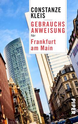 Das Buchcover zeigt eine moderne Stadtszene mit hohen, gläsernen Wolkenkratzern, die in den Himmel ragen, und historischen Gebäuden im Vordergrund. Der Himmel wirkt hellblau und strahlt eine freundliche Atmosphäre aus. Der Titel „Gebrauchsanweisung für Frankfurt am Main“ ist in großer, roter Schrift deutlich sichtbar, während der Name der Autorin „Constanze Kleis“ in schwarzer Schrift darüber platziert ist. Die Verwendung von typografischen Kontrasten verleiht dem Cover Dynamik.