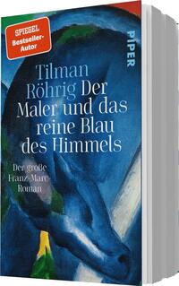 Das Buchcover zeigt eine lebhafte und expressive Malerei in Blau- und Grüntönen, die eine Atmosphäre von Kreativität und Tiefe vermittelt. Im Vordergrund sind geschwungene Linien und Formen, die an die Werke von Franz Marc erinnern. Der Titel „Der Maler und das reine Blau des Himmels“ ist in eleganter, weißer Schrift platziert, zusammen mit dem Namen des Autors Tilman Röhrig. Oben links ist ein rotes Etikett mit der Aufschrift „SPIEGEL-Bestseller-Autor“ zu sehen. Am unteren Rand steht der Zusatz „Der große Franz-Marc-Roman“ in kleinerer Schrift.