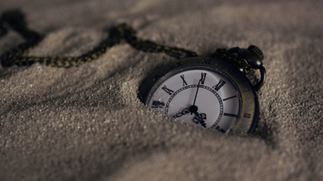 Eine Taschenuhr liegt halb im Sand vergraben