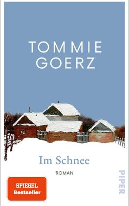 Das Buchcover zeigt eine winterliche Landschaft mit mehreren kleinen, verschneiten Holzhausern vor einem hellblauen Himmel. Die Häuser sind in sanften Erdtönen gehalten, was ihnen einen rustikalen Charme verleiht. Mittig steht der Titel „Im Schnee“ in eleganter, weißer Schrift, darunter ist das Wort „Roman“ in kleinerer Schriftgröße platziert. Oben steht der Name des Autors Tommie Goerz in größerer, klarer Schrift. In der unteren Ecke befindet sich ein rotes Feld mit dem Text „SPIEGEL Bestseller“.