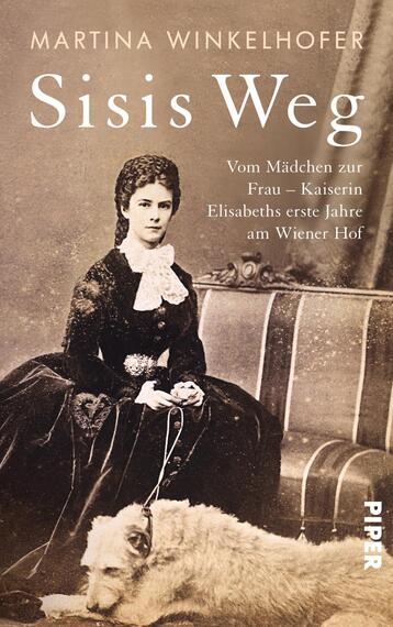 Das Buchcover zeigt eine historische Fotografie einer jungen Frau in eleganter, schwarzer Kleidung mit einem weißen Kragen und einer Hochsteckfrisur. Sie sitzt auf einem Stuhl und legt ihren Arm auf einen Hund. Der Hintergrund ist neutral und hell gehalten. Der Titel „Sisis Weg“ steht in großen, weißen Buchstaben oben, während der Untertitel „Vom Mädchen zur Frau – Kaiserin Elisabeths erste Jahre am Wiener Hof“ in kleinerer Schrift darunter platziert ist. Der Name der Autorin, Martina Winkelhofer, befindet sich oben links.