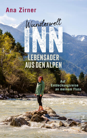 Das Buchcover zeigt eine Frau in grüner Jacke, kniehoch auf Felsen im fließenden, hellen Gebirgsfluss stehend, im Hintergrund bewaldete Hänge und schneebedeckte Alpengipfel unter hellem Himmel. Oben links steht der Autorname „Ana Zirner“ in roter Schrift, mittig groß der Titel „Wunderwelt INN“ mit kräftiger, strukturierter Weißschrift, darunter in weißer und gelber Sans-Serif-Schrift „Lebensader aus den Alpen“ und klein „Auf Entdeckungsreise an meinem Fluss“.