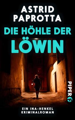 Das Buchcover zeigt einen dunklen, schmalen Straßenabschnitt, der von hohen Gebäuden flankiert wird. Eine schwarz gekleidete Person mit umgedrehter Kapuze steht im Vordergrund und blickt in die Gasse. Der Titel „DIE HÖHLE DER LÖWIN“ ist in kräftigem Türkis hervorgehoben, während der Autorenname „ASTRID PAPROTTA“ in weißer Schrift darüber platziert ist. Unten rechts befindet sich das Logo des Verlags Piper in blau. Die gesamte Atmosphäre vermittelt Spannung und Geheimnis.