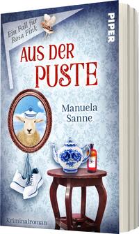 Das Buchcover zeigt einen hellblauen Hintergrund mit einem zarten, floralen Muster. In der oberen Mitte steht der Titel „AUS DER PUSTE“ in großen, roten Buchstaben. Darunter ist der Schriftzug „Manuela Sanne“ zu sehen. Im Hintergrund befindet sich ein ovales Bild eines Schafs mit einem blauen Hut. Vorn sind ein altes Porzellanobjekt und ein rotes Fläschchen zu erkennen, ergänzt durch einen Paar Sportschuhe. Die Gesamtatmosphäre ist humorvoll und geheimnisvoll, passend zum Kriminalroman.
