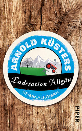 Das Buchcover zeigt einen runden, kreisförmigen Ausschnitt vor einem rustikalen Holzuntergrund. Der obere Teil ist in einem strahlenden Blau gehalten und trägt den Schriftzug „ARNOLD KÜSTERS“ in weißen, gut lesbaren Buchstaben. Unterhalb des blauen Abschnitts steht der Titel „Endstation Allgäu“ in schwarzer Schrift auf einem weißen Banner. Darunter befindet sich die Aufschrift „KRIMINALROMAN“ in kleinerer, ebenfalls schwarzer Schrift. Im Zentrum ist eine Landschaft mit einem Traktor und schneebedeckten Bergen angedeutet, was eine ländliche, spannende Atmosphäre vermittelt.
