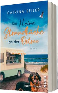 Das Buchcover zeigt eine sonnige Meeresküste mit blauem Himmel, Möwe im Flug und Wellen an einem Sandstrand; links ein pastellgrüner Imbisswagen mit offenem Fenster und Markise, vorne auf dem Weg ein fröhlicher Dackel. Titel in großer Typografie: oben „CATRINA SEILER“, mittig „Die kleine Strandküche an der Ostsee“ in einer Kombination aus serifenloser und handschriftlicher, orangefarbener Schrift; unten kleingedruckt „ROMAN“.