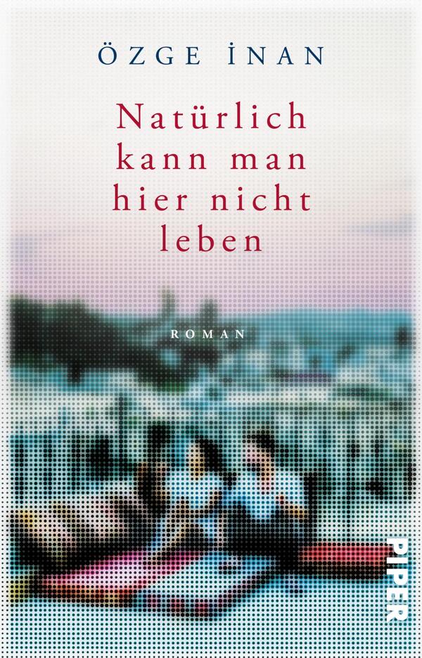 Das Buchcover zeigt eine unscharfe, verträumte Szenerie mit zwei Figuren, die auf einem Teppich sitzen und den Blick auf eine Stadtlandschaft richten. Der Hintergrund ist in sanften Rosa- und Blautönen gehalten, was eine melancholische Atmosphäre vermittelt. Der Titel „Natürlich kann man hier nicht leben“ ist zentral in kräftigem Rot platziert, während der Autorennamen „Özge İnan“ in einem eleganten dunklen Blau oben steht. Der Untertitel „Roman“ ist dezent in Kleinbuchstaben abgedruckt.