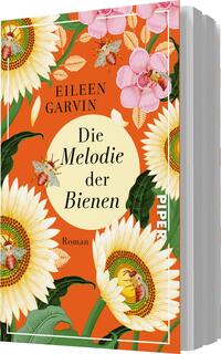 Das Buchcover zeigt eine leuchtend orangefarbene Hintergrundfläche, die mit großen, detailliert gezeichneten Sonnenblumen und floralen Elementen in Pink und Weiß gestaltet ist. In der Mitte befindet sich ein ovales, helles Feld mit dem Titel „Die Melodie der Bienen“ in eleganter schwarzer Schrift. Oben links steht der Name der Autorin Eileen Garvin in einer klaren Schriftart. Einige kleine Bienen und Blüten ergänzen das lebendige Design und vermitteln eine fröhliche, naturverbundene Atmosphäre.