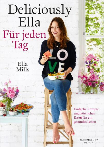Das Buchcover zeigt eine freundliche, lächelnde Frau mit langen, braunen Haaren, die auf einem Hocker sitzt. Sie trägt ein schwarzes Sweatshirt mit dem Wort „LOVE“ in bunten Buchstaben und Jeans. In ihren Händen hält sie ein Stück Wassermelone und eine Schale mit frischen Zutaten. Der Hintergrund zeigt eine helle, gemusterte Mauer und Blumenarrangements. Oben steht der Titel „Deliciously Ella“ und darunter „Für jeden Tag“ in eleganter Schrift. Am unteren Rand sind die Worte „Einfache Rezepte und köstliches Essen für ein gesundes Leben“ zu lesen. Autorin ist Ella Mills.