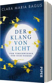 Das Buchcover zeigt einen tiefblauen Hintergrund mit einer großen, leuchtend weißen Kreisscheibe, die den Titel „DER KLANG VON LICHT“ umgibt. Der Titel ist in einer eleganten, kräftigen Schrift in Blau gehalten, darüber steht der Name der Autorin, „CLARA MARIA BAGUS“, in einer schlichten weißen Schrift. Gelbe Silhouetten von fliegenden Vögeln umrahmen die Kreisscheibe und erzeugen eine fühlbare Dynamik. Darunter ist der Untertitel „VOM VERSCHWINDET UND SICH-FINDEN“ in kleinerer Schrift positioniert, und am unteren Rand ist das Verlagslogo „PIPER“ platziert.