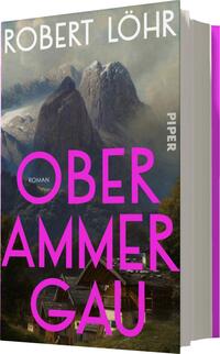Das Buchcover zeigt eine eindrucksvolle Landschaft mit majestätischen Bergen im Hintergrund und einer malerischen Siedlung im Vordergrund. Die Farbpalette reicht von sanften Blau- und Grautönen bis zu kräftigem Pink. Der Titel „OBERAMMERGAU“ ist in großen, auffälligen Buchstaben in Pink gesetzt und sticht hervor, während der Untertitel „Roman“ kleiner darunter steht. Der Autor, Robert Löhr, ist in einer klaren Schriftart am oberen Rand platziert. Die Gesamtatmosphäre vermittelt eine Verbindung zur Natur und zur klassischen Literatur.