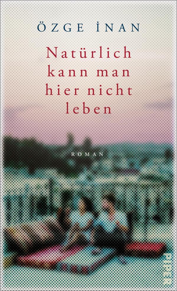 Das Buchcover zeigt im Hintergrund eine unscharfe Stadtsilhouette bei Dämmerung in sanften Blau- und Rosa-Tönen. Im Vordergrund sitzen zwei Personen auf einer matten Fläche, umgeben von bunten Kissen. Der Titel „Natürlich kann man hier nicht leben“ ist in kräftigem Rot zentriert und prägnant platziert, während der Name der Autorin, Özge İnan, oben in einfacher Schrift steht. Die Atmosphäre vermittelt eine Mischung aus Nachdenklichkeit und Intimität.