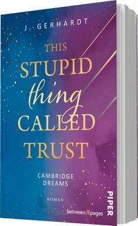 Das Buchcover zeigt einen Farbverlauf von Lila zu Blau und Rosa, angereichert mit goldenen Glitzerpunkten. In der oberen Hälfte steht in großen, eleganten Buchstaben „THIS STUPID thing CALLED TRUST“ in Gold, während darunter in kleinerer Schrift „CAMBRIDGE DREAMS“ und „ROMAN“ in Weiß zu sehen sind. Eine dynamische Linie zieht sich diagonal über das Cover. Die insgesamt verspielte und träumerische Atmosphäre wird durch die Farbauswahl und Gestaltung der Typografie verstärkt.