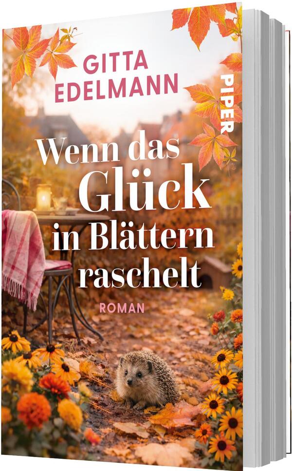 Das Buchcover zeigt eine warme, herbstliche Szene in Orange- und Goldtönen mit fallenden Blättern. Im Vordergrund liegt ein Igel zwischen bunten Blumen und Laub, dahinter ein Stuhl mit rosa-kariertem Plaid und eine Laterne. Der Titel „Wenn das Glück in Blättern raschelt“ ist groß, weiß und serifenbetont, der Autorenname Gitta Edelmann steht oben in Versalien, pinkfarben. Stimmung: gemütlich, nostalgisch.