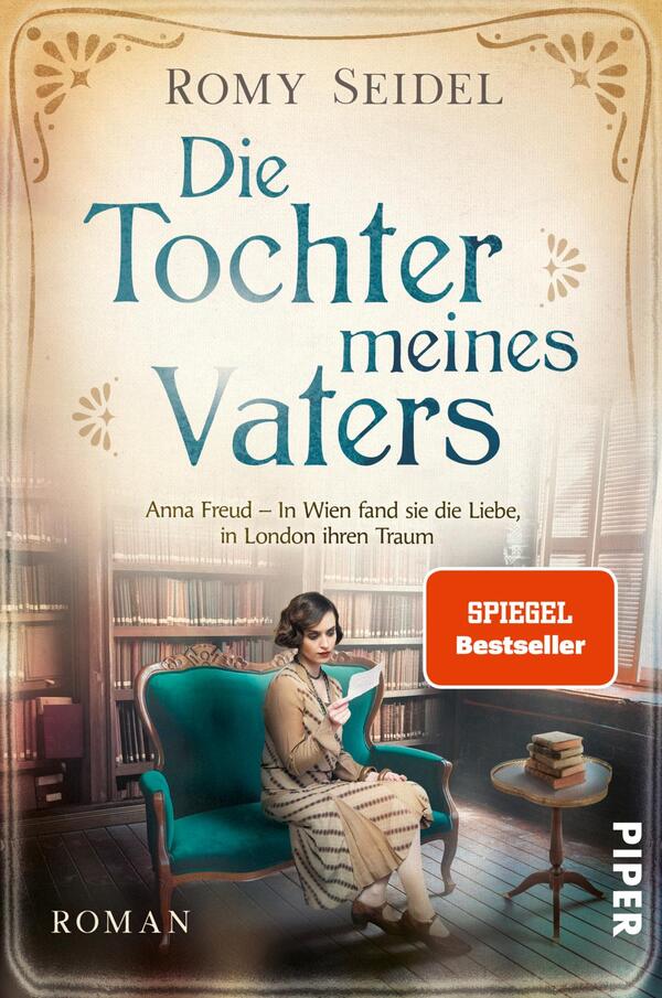 Das Buchcover zeigt eine junge Frau in einem eleganten, blauen Kleid, die auf einem Sessel sitzt und ein Buch liest. Sie hat dunkle, gelockte Haare und wirkt nachdenklich. Der Hintergrund besteht aus einer Bücherwand, die eine gemütliche Atmosphäre vermittelt. Der Titel „Die Tochter meines Vaters“ ist in geschwungener, blauer Schrift über der Protagonistin platziert. Darunter steht „Anna Freud – In Wien fand sie die Liebe, in London ihren Traum“ in kleinerer Schrift. Ein rotes Label weist auf „SPIEGEL Bestseller“ hin.