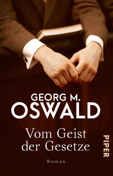 Das Buchcover zeigt die Hände eines Mannes in einem Anzug, die auf einem Tisch ruhen. Der Hintergrund ist in einem warmen Braunton gehalten, der eine seriöse Atmosphäre erzeugt. In der oberen Drittel des Covers steht der Autorennamen „Georg M. Oswald“ in einer eleganten, serifenlosen Schrift. Darunter befindet sich der Titel „Vom Geist der Gesetze“ in weißer Schrift, die sich klar vom Hintergrund abhebt. Im unteren rechten Bereich ist das Verlagslogo „PIPER“ in einer dezenten Größe platziert.