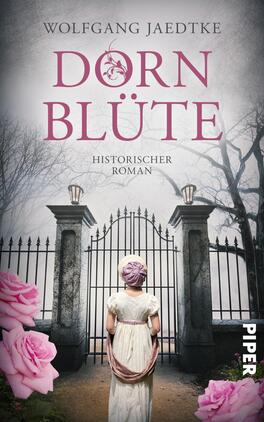 Das Buchcover zeigt eine atmosphärische Szenerie mit einem großen, eleganten Tor, das von hohen, verschneiten Bäumen flankiert wird. Im Vordergrund steht eine junge Frau in historischer Kleidung mit einem lila Hut. Sie blickt auf das Tor, das eine geheimnisvolle Stimmung erzeugt. Der Titel „DORNBLÜTE“ ist in großen, geschwungenen, rosa Buchstaben platziert, während der Untertitel „Historischer Roman“ in schlichterer Schrift darunter steht. Rosa Blumen sind im unteren Teil des Covers sichtbar, was eine sanfte Farbgebung ergänzt.