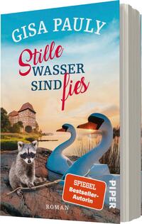Das Buchcover zeigt eine idyllische Landschaft mit einem ruhigen Gewässer im Vordergrund. Zwei stilisierte Schwäne schwimmen sanft auf dem Wasser. Ein Waschbär sitzt am Ufer und schaut neugierig in die Richtung des Betrachters. Im Hintergrund ist ein altes, charmantes Gebäude in warmen Farben zu sehen. Der Titel „Stille Wasser sind fies“ ist in auffällig roter Schrift gestaltet, während der Autorennamen „Gisa Pauly“ darüber in geschwungener, blauer Typografie steht. Die Atmosphäre wirkt friedlich und gleichzeitig mysteriös.