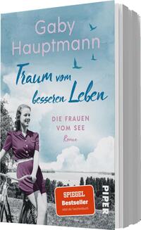 Das Buchcover zeigt eine Frau auf einem Fahrrad vor einer idyllischen Szenerie am Wasser, umgeben von einer sanften Landschaft. Der Himmel ist bläulich mit vereinzelt schwebenden Vögeln. Die Farbgestaltung ist hell und freundlich, dominiert von Blau- und Rosatönen. Der Titel „Traum vom besseren Leben“ ist in eine auffällige, kursive Schrift gesetzt, während der Autorinnenname „Gaby Hauptmann“ darüber schwebt. Unter dem Titel steht „DIE FRAUEN VOM SEE“ in klarer, serifenloser Typografie. Ein orangefarbener Button auf dem Cover hebt den Zusatz „SPIEGEL Bestseller“ hervor, sowie den Hinweis „Jetzt als Taschenbuch“.