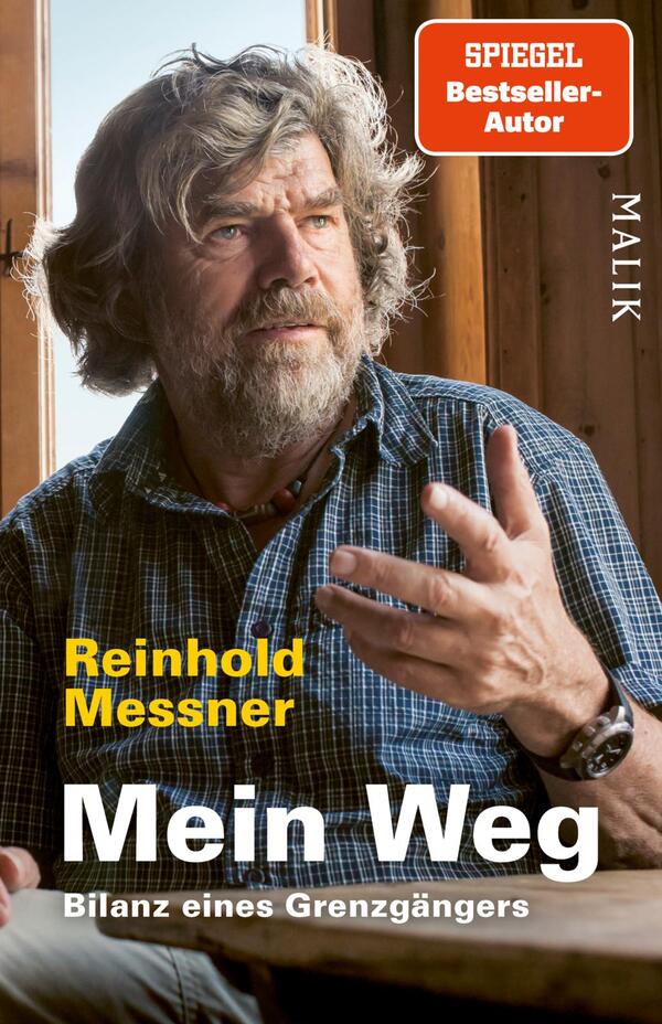 Das Buchcover zeigt Reinhold Messner in einem natürlichen Licht, während er in einem Holzraum sitzt. Sein ausdrucksvolles Gesicht und der leicht nachdenkliche Blick verstärken die persönliche Atmosphäre. Er trägt ein karierter Hemd und zeigt mit der Hand eine gestische Geste. Der Titel „Mein Weg“ ist in großer, gelber Schrift hervorgehoben, gefolgt von dem Untertitel „Bilanz eines Grenzgängers“. Oben rechts befindet sich ein rotes Quadrat mit der Aufschrift „SPIEGEL Bestseller-Autor“. Die Gestaltung vermittelt eine Mischung aus Authentizität und Reflexion.