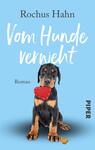 Das Buchcover zeigt einen niedlichen Rottweiler-Welpen, der auf einem hellblauen Hintergrund sitzt. Der Hund hält ein rotes Herzspielzeug im Mund und hat eine verspielte Ausstrahlung. Der Titel „Vom Hunde verweht“ ist in einer freundlichen, handschriftlichen Schriftart in Weiß und gut lesbar platziert. Darunter steht das Wort „Roman“ in einer schlichten Schrift. Unten rechts ist das Logo des Verlags „PIPER“ in Schwarz abgedruckt.