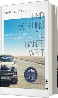 Das Buchcover zeigt einen blauen Himmel über einer weiten Straße, die sich in die Ferne erstreckt. In der unteren Ecke ist ein alter, schwarzer Wagen abgebildet. Der Titel „UND VOR UNS DIE GANZE WELT“ steht in großen, leicht versetzten Buchstaben, während der Untertitel „Eine Reise über Land von Indien in die Schweiz“ kleiner darunter platziert ist. Das Cover vermittelt eine Mischung aus Abenteuer und Fernweh. Unten links befindet sich ein runder Button mit dem Text „30 Jahre MALIK“.