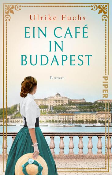 Das Buchcover zeigt eine Frau in einem eleganten, historischen Kleid mit einer türkisfarbenen Rockpartie und einem weißen Oberteil. Sie steht mit dem Rücken zur Betrachterin am Ufer einer Wasserfläche, im Hintergrund sind monumentale Gebäude und eine sanfte Hügellandschaft von Budapest zu sehen. Der Titel „Ein Café in Budapest“ ist in großen, hellblauen Buchstaben mittig platziert, darüber der Name der Autorin „Ulrike Fuchs“ in einem zarten Rot. Die Atmosphäre strahlt Ruhe und Nostalgie aus.
