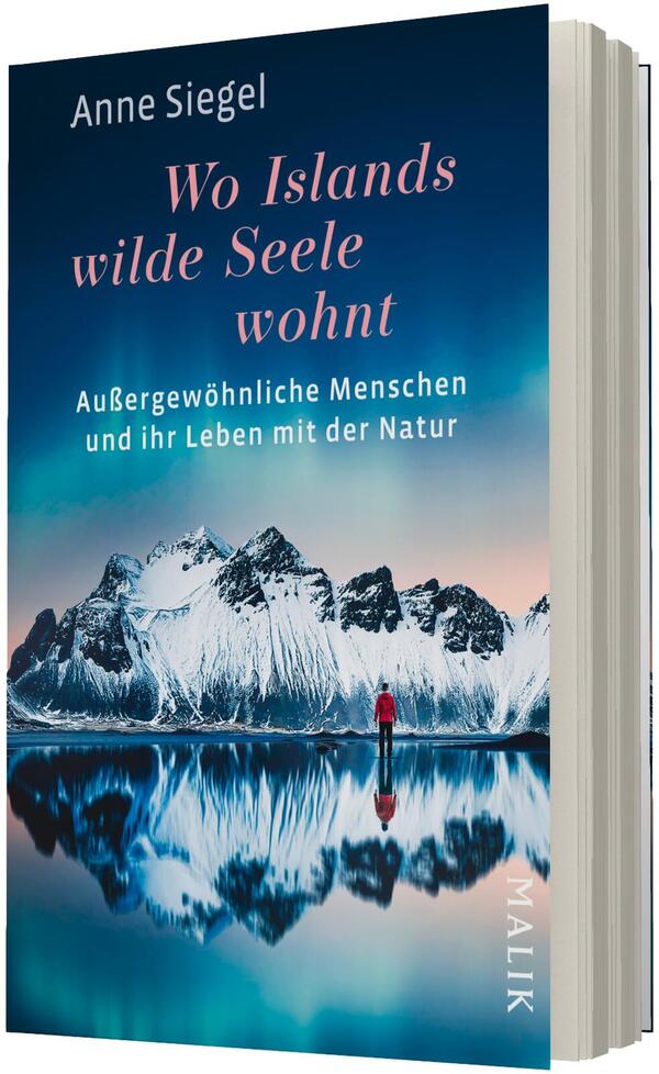 Das Buchcover zeigt eine Person in rotem Mantel, die an einem stillen Seeufer steht und auf schroffe, schneebedeckte Berge blickt, deren Spiegelung das Wasser klar wiedergibt. Farbpalette in Blau-, Türkis- und Rosatönen mit dunklem Himmel. Titel „Wo Islands wilde Seele wohnt“ in großer, hellrosa Serifenschrift; Untertitel „Außergewöhnliche Menschen und ihr Leben mit der Natur“ in weißer Grotesk. Oben links Urhebername „Anne Siegel“.