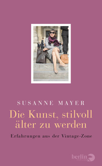 Das Buchcover zeigt einen sanften lila Hintergrund, vor dem ein zentrales, quadratisches Porträt einer eleganten Frau sitzt. Sie trägt eine modische Sonnenbrille und einen schicken Schal, während sie selbstbewusst auf einer Treppe posiert. Über dem Bild steht in klaren, modernen Buchstaben der Name „Susanne Mayer“. Der Titel „Die Kunst, stilvoll älter zu werden“ ist in einer goldenen, serifenlosen Schrift dargestellt, ergänzt durch den Untertitel „Erfahrungen aus der Vintage-Zone“ in einfacher Schrift darunter.